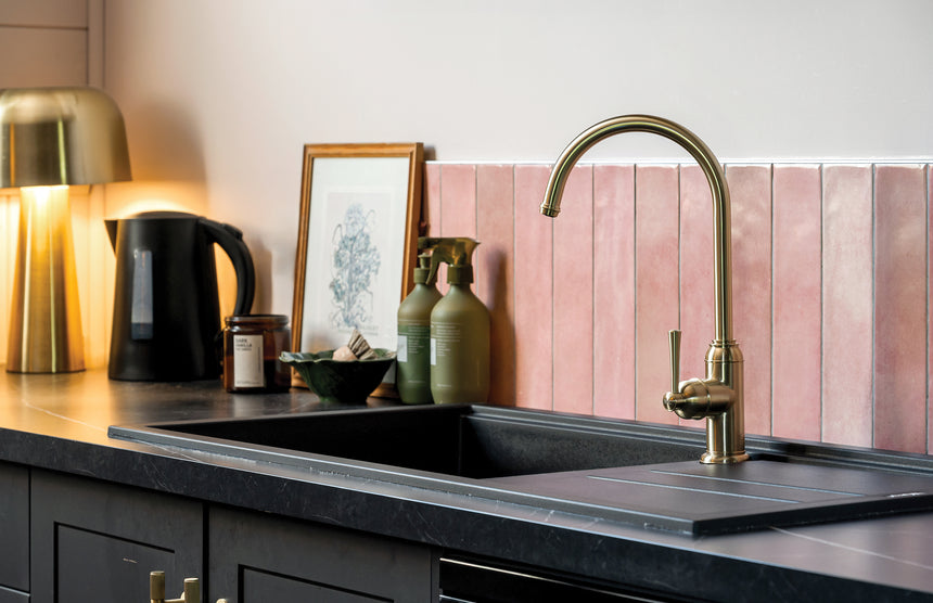 Phoenix Cromford brushed gold sink mixer installed on dark countertop above black sink with pink tile splashback by Tilemall