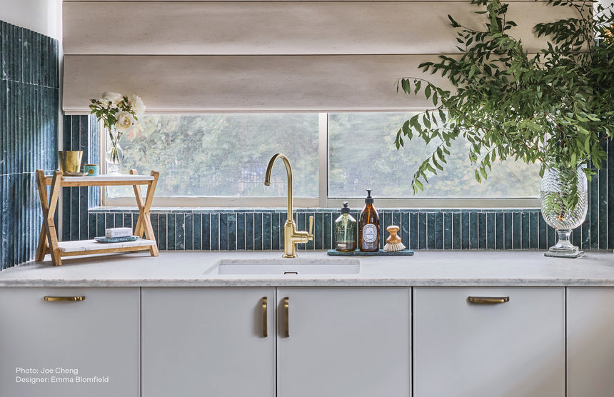 Phoenix Cromford brushed gold sink mixer installed on light countertop above white sink with dark tile splashback by Tilemall